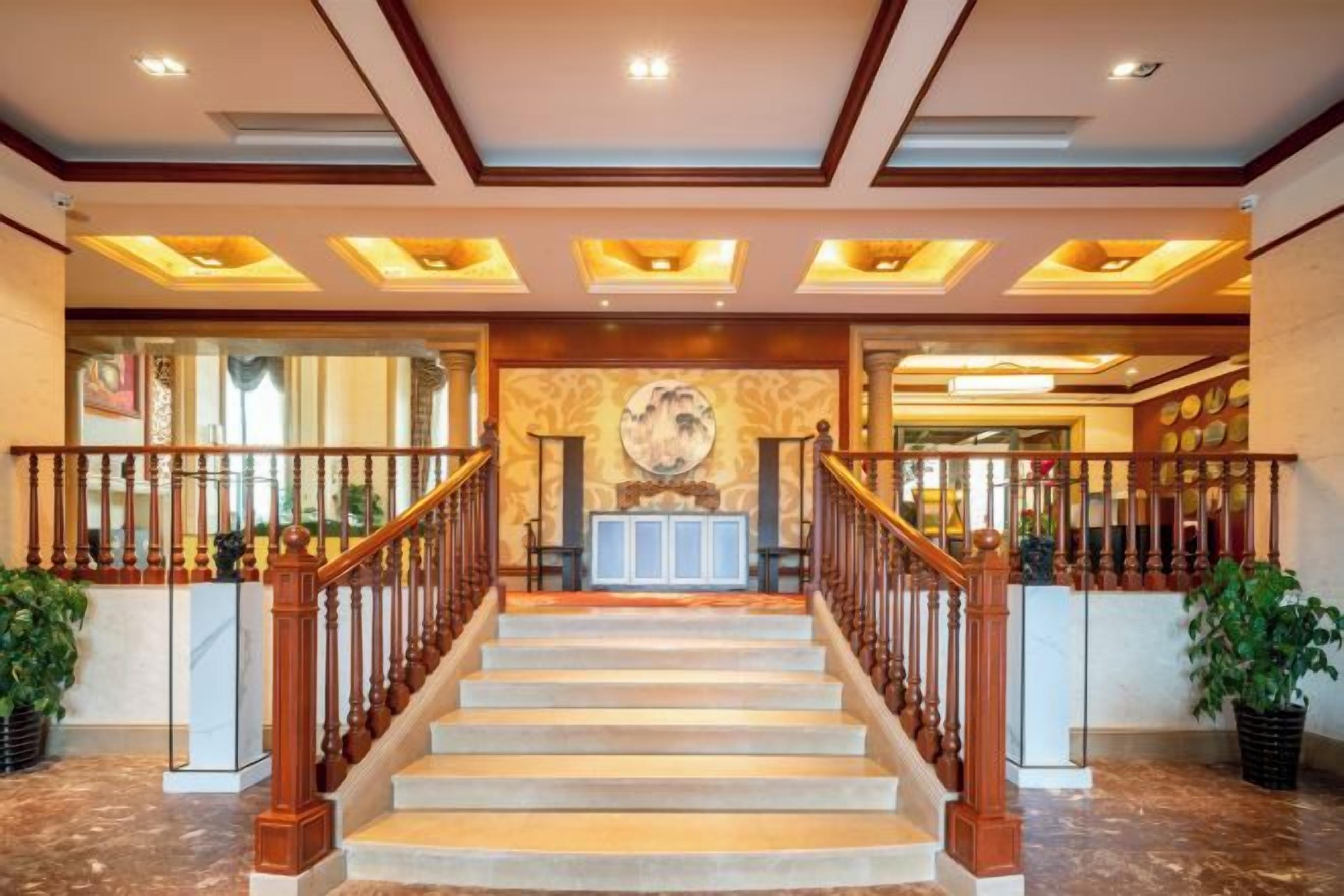 Un grand escalier en bois, doté d’une rampe, mène à un espace d’accueil comprenant un bureau et des chaises.
