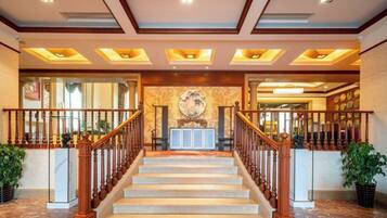 Un grand escalier en bois, doté d’une rampe, mène à un espace d’accueil comprenant un bureau et des chaises.