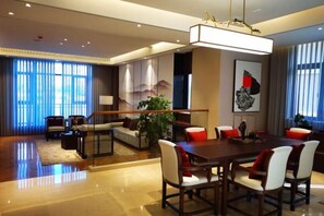 A modern hotel dining area with a large wooden table, comfortable seating, and a large window offering a view. - Aile Holiday Hotel (Sanming)