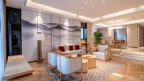 A modern living room with a sofa, chairs, a coffee table, and a lamp. There is a large painting on the wall and a plant in the corner. - Aile Holiday Hotel (Sanming)
