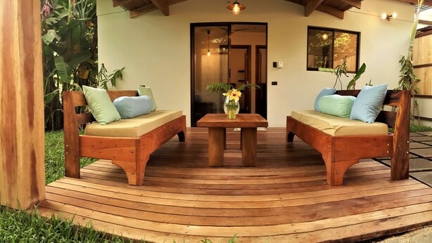 A wooden deck with two sofas and a table, surrounded by greenery.