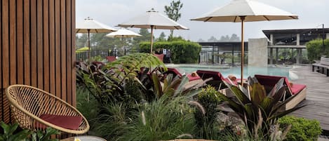 A poolside area with wicker chairs, umbrellas, and lush greenery.