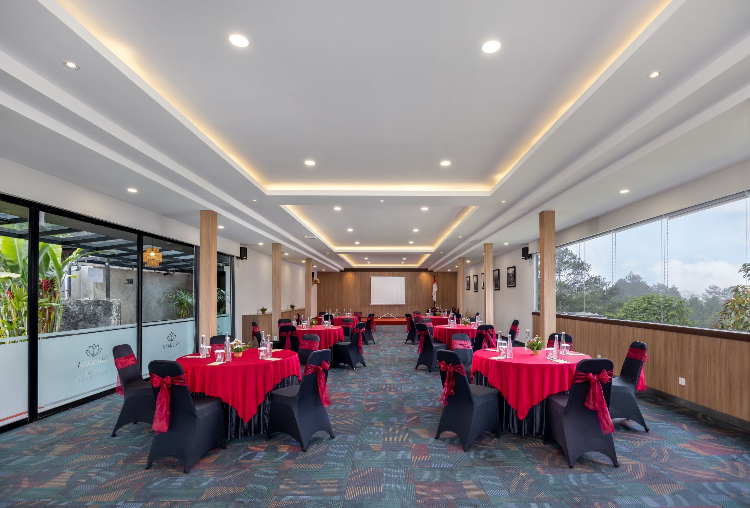 A conference room with multiple tables, black chairs with red sashes, and a large screen at the front.