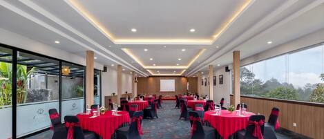 A conference room with multiple tables, black chairs with red sashes, and a large screen at the front.