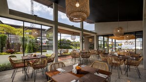 Een restaurant met grote ramen, rieten meubels en hangende rotanlampen.