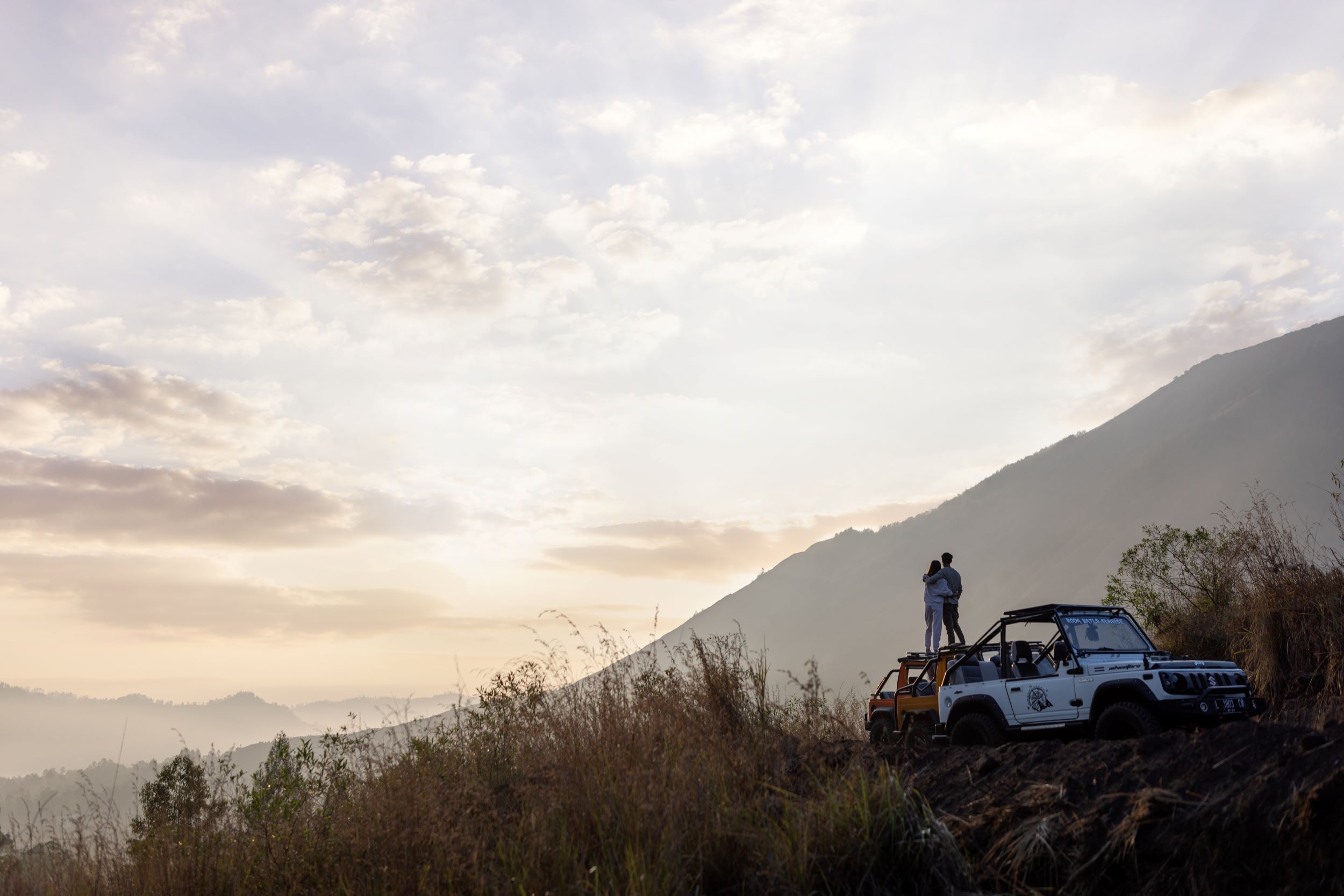 A white off-road vehicle parked on a grassy hill with a mountainous backdrop.