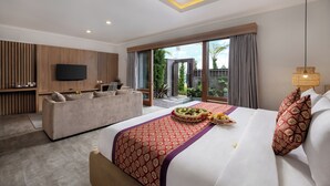 Een moderne hotelkamer met een groot bed, een bank, een flatscreen televisie en een balkon met uitzicht op groen.