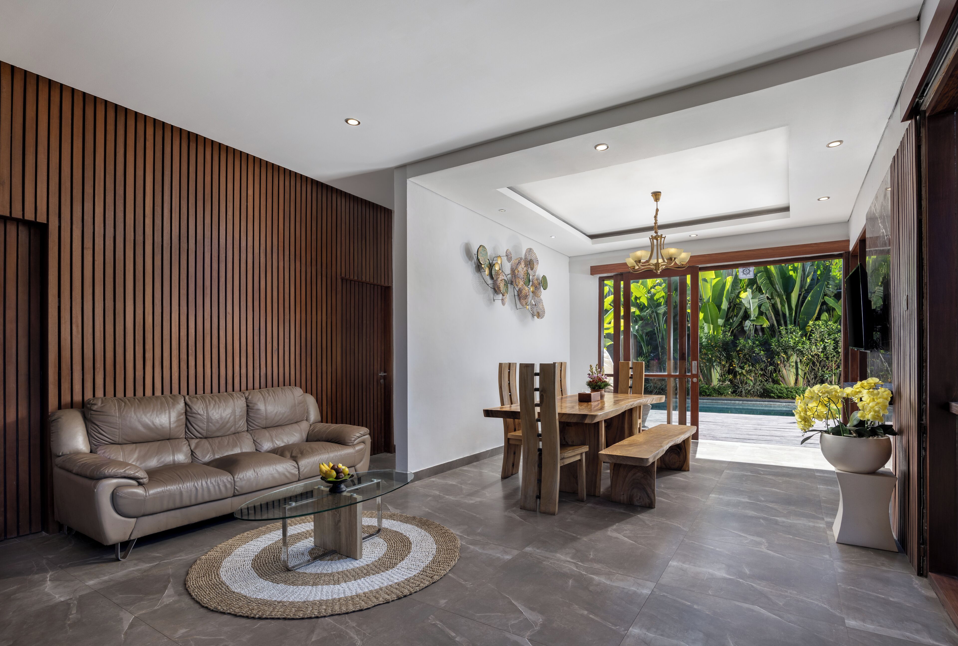Una sala moderna con un sofá de cuero, una mesa de comedor de madera y sillas, una mesa de centro de vidrio y vistas a zonas verdes a través de amplios ventanales.