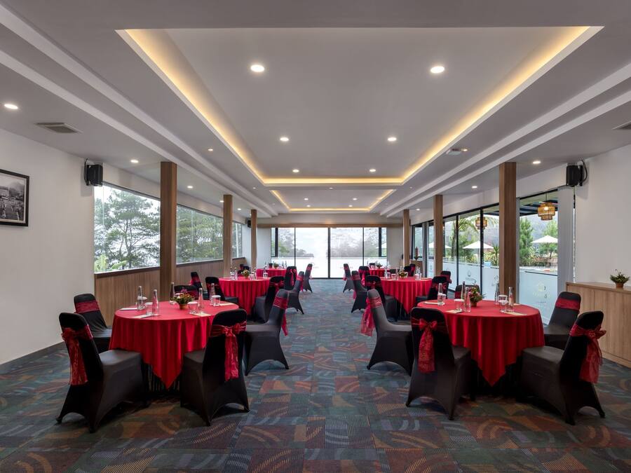 Een congrescentrum met ronde tafels, rode tafelkleden, zwarte stoelen en een kamerbreed tapijt met een patroon.
