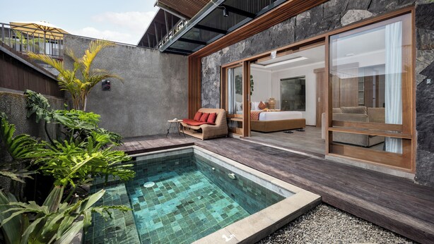 Een modern buitenzwembad met een stenen muur, een houten terras en een glazen slaapkamer.