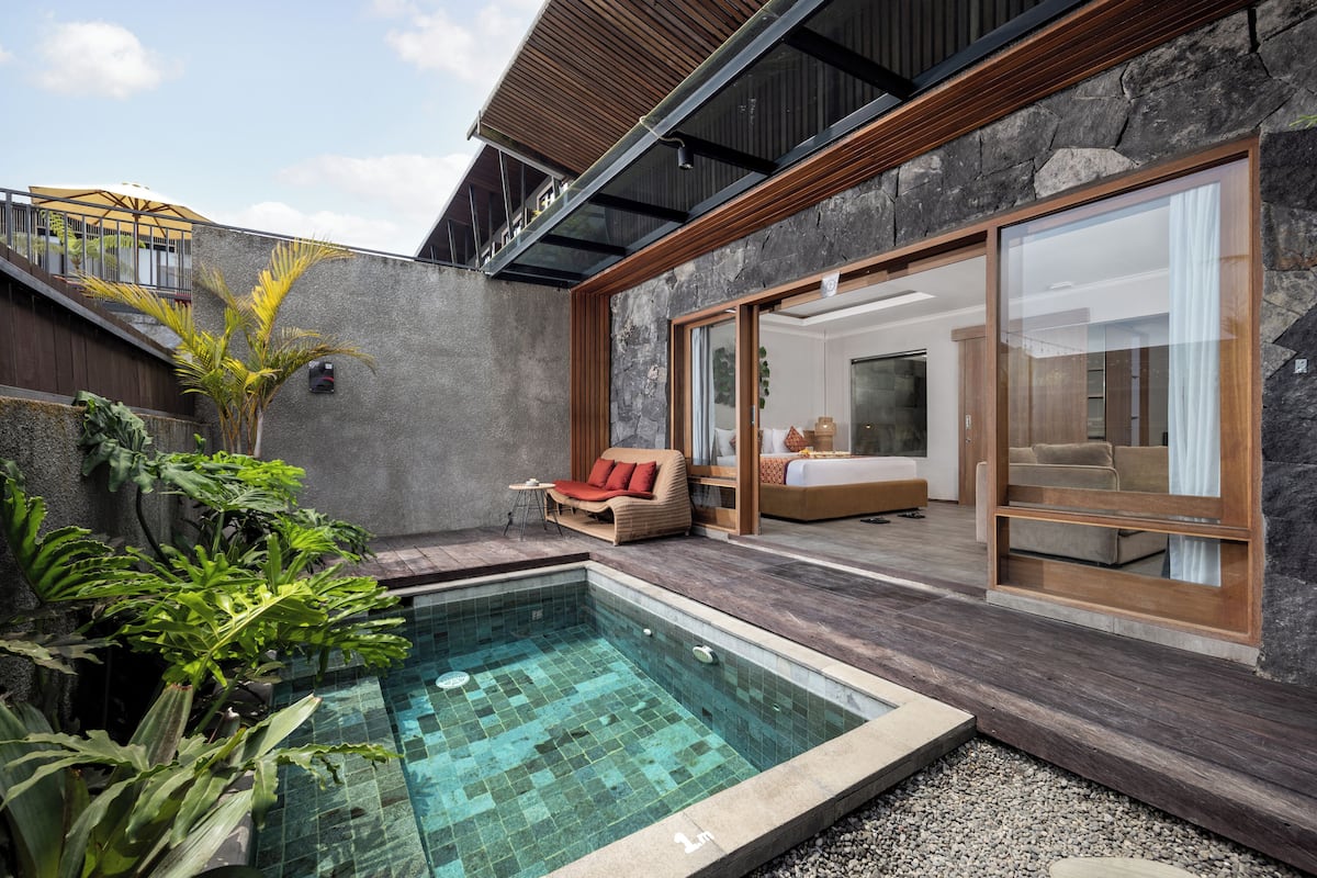 Een modern buitenzwembad met een stenen muur, een houten terras en een glazen slaapkamer.