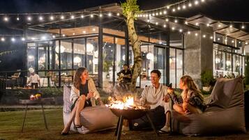 An outdoor seating area with a fire pit, surrounded by string lights and modern architecture.