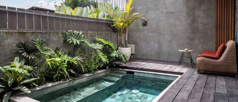 A swimming pool with tiled edges, surrounded by various plants and a wooden deck.