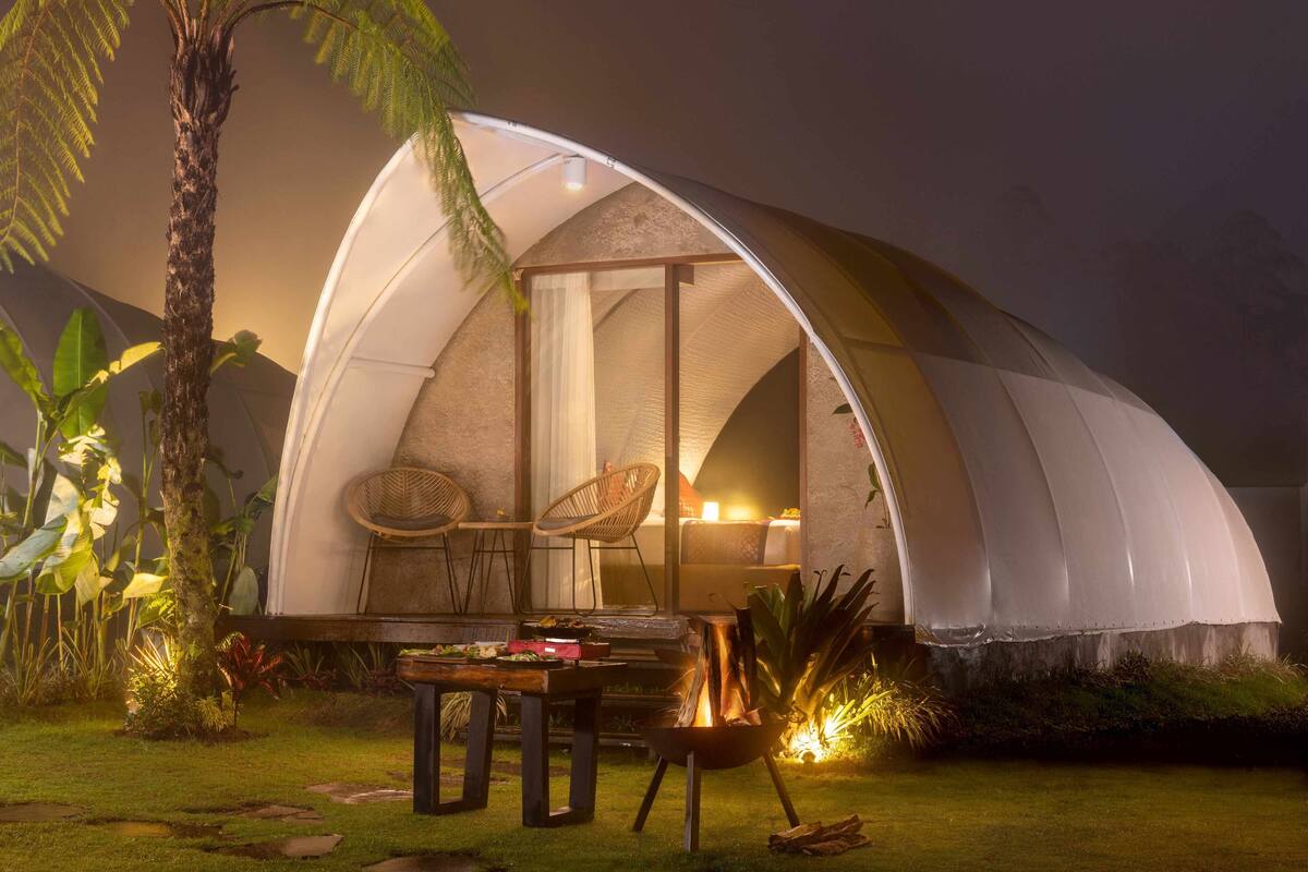 Een koepeltent met een tafel en stoelen buiten, omringd door tropische planten.
