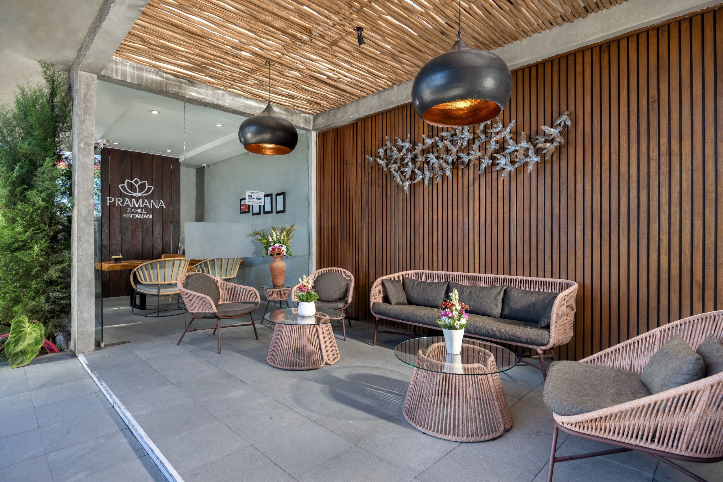 A modern outdoor seating area with wicker furniture, a glass coffee table, and a decorative wall with vertical wooden slats.