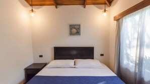A bedroom with a bed, a nightstand, a painting on the wall, and a window with curtains.