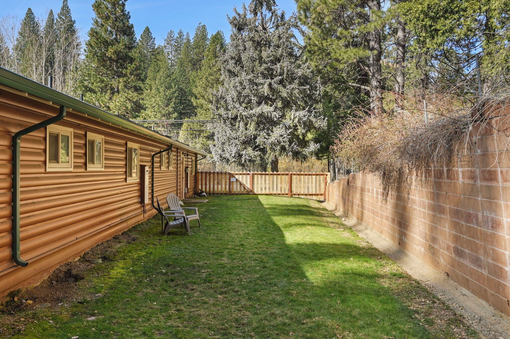 A wooden cabin with a fenced backyard, a lawn, and a wooden deck.