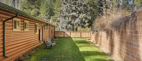 A wooden cabin with a fenced backyard, a lawn, and a wooden deck.