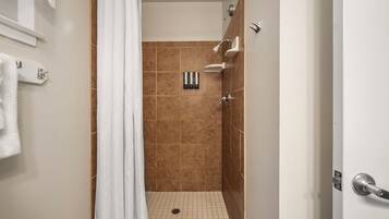 Un bagno con doccia, pareti piastrellate, un asciugamano bianco e una tenda da doccia.