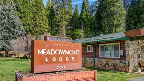 A wooden sign for Meadowmont Lodge with a stone building in the background. - Arnold Meadowmont Lodge (Arnold)