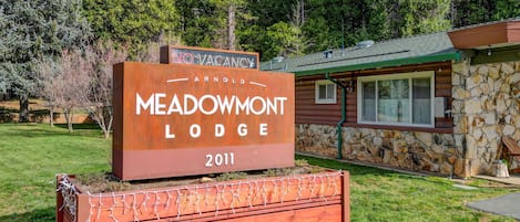 A wooden sign for Meadowmont Lodge with a stone building in the background.