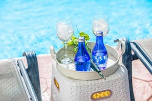 A poolside setting with a beverage cooler containing two blue bottles and two glasses with ice.
