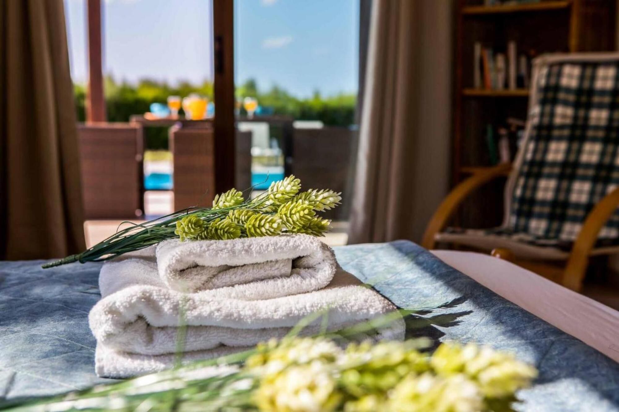 Ordentlich gefaltetes Handtuchset auf einem Bett mit Blick auf einen Pool und eine Außenlounge.