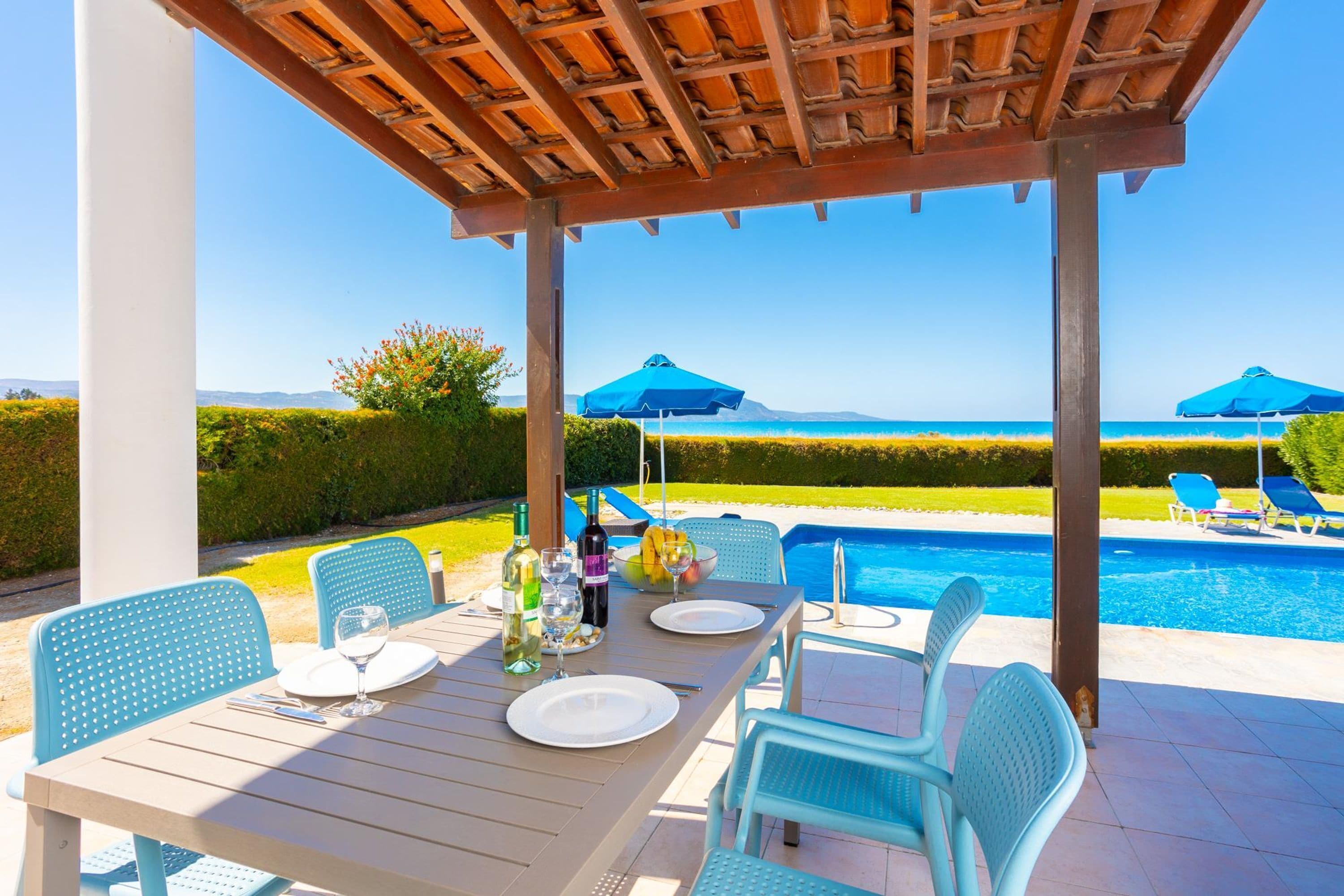 A poolside dining area with a wooden pergola, outdoor seating, and a view of the pool and ocean.