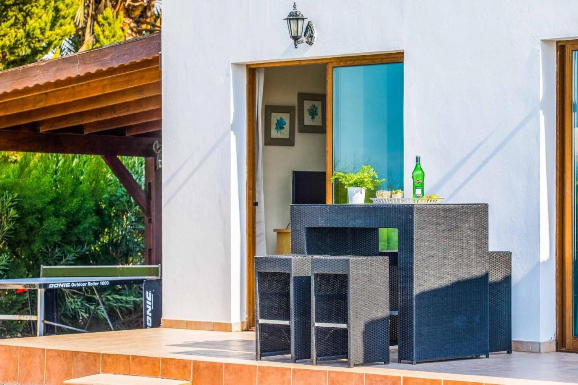 A patio area with a wicker table and chairs, a potted plant, and a bottle of liquor.