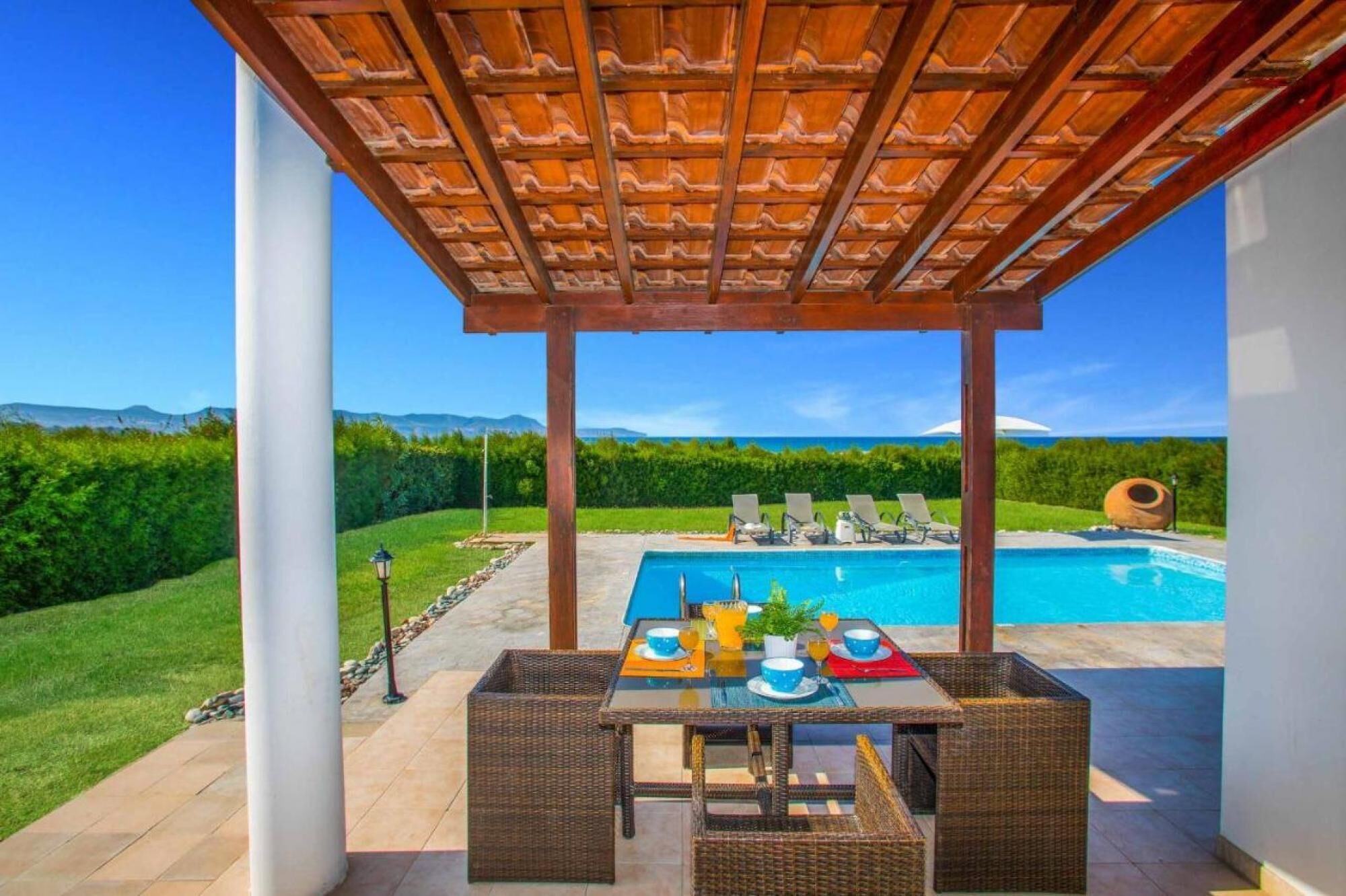 Un espace extérieur abrité comprenant une piscine, des chaises longues et une table dressée pour les repas.