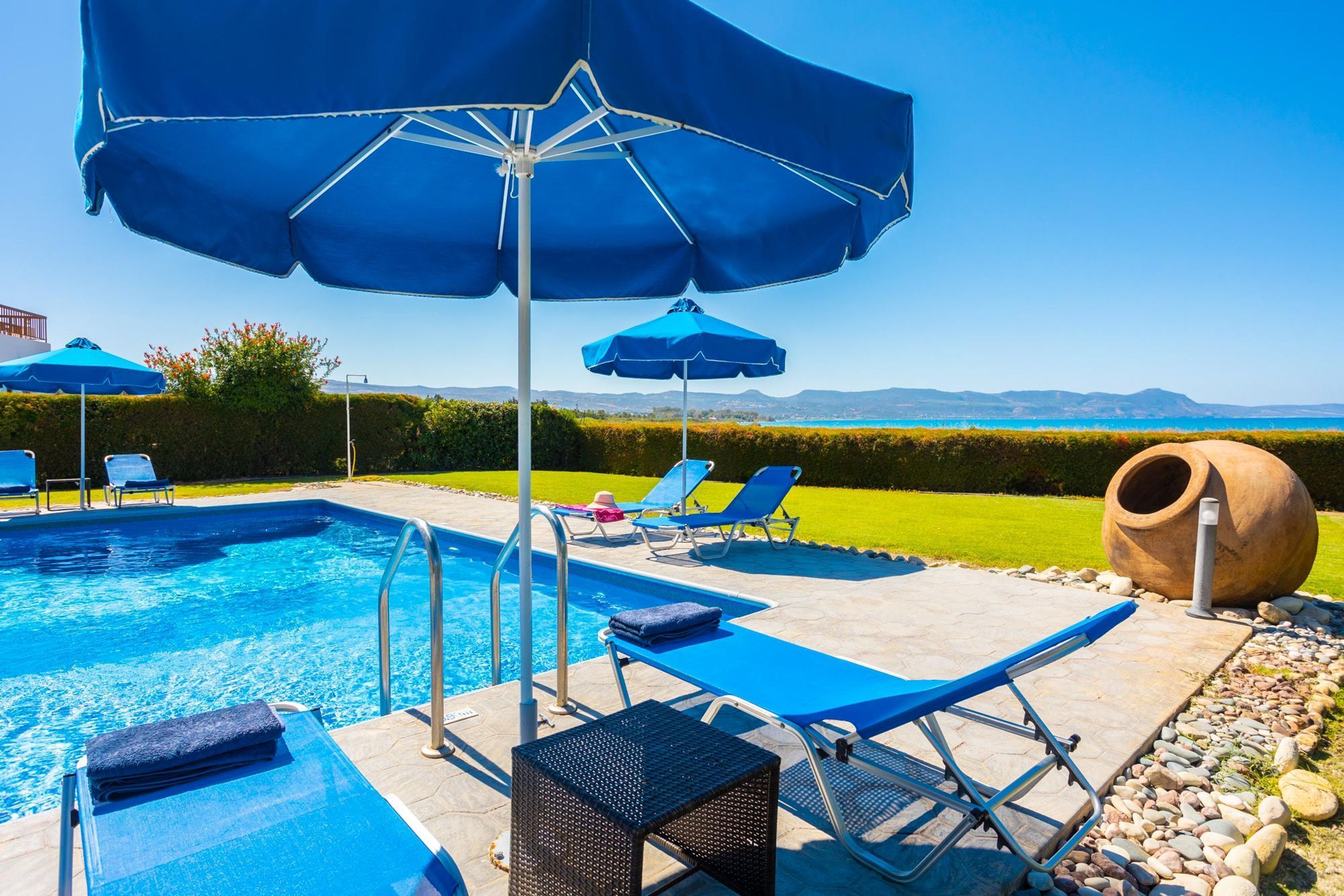 Une piscine dotée de chaises longues et de parasols, entourée d’un jardin aménagé et offrant une vue sur des collines lointaines.