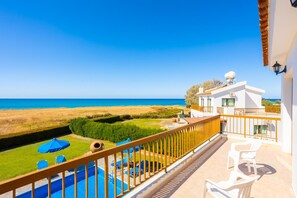Uma varanda com vista para o mar, uma piscina e um edifício branco com antena parabólica.