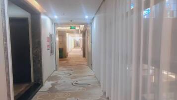 A hotel corridor with a patterned carpet, a door on the left, and a curtain on the right.