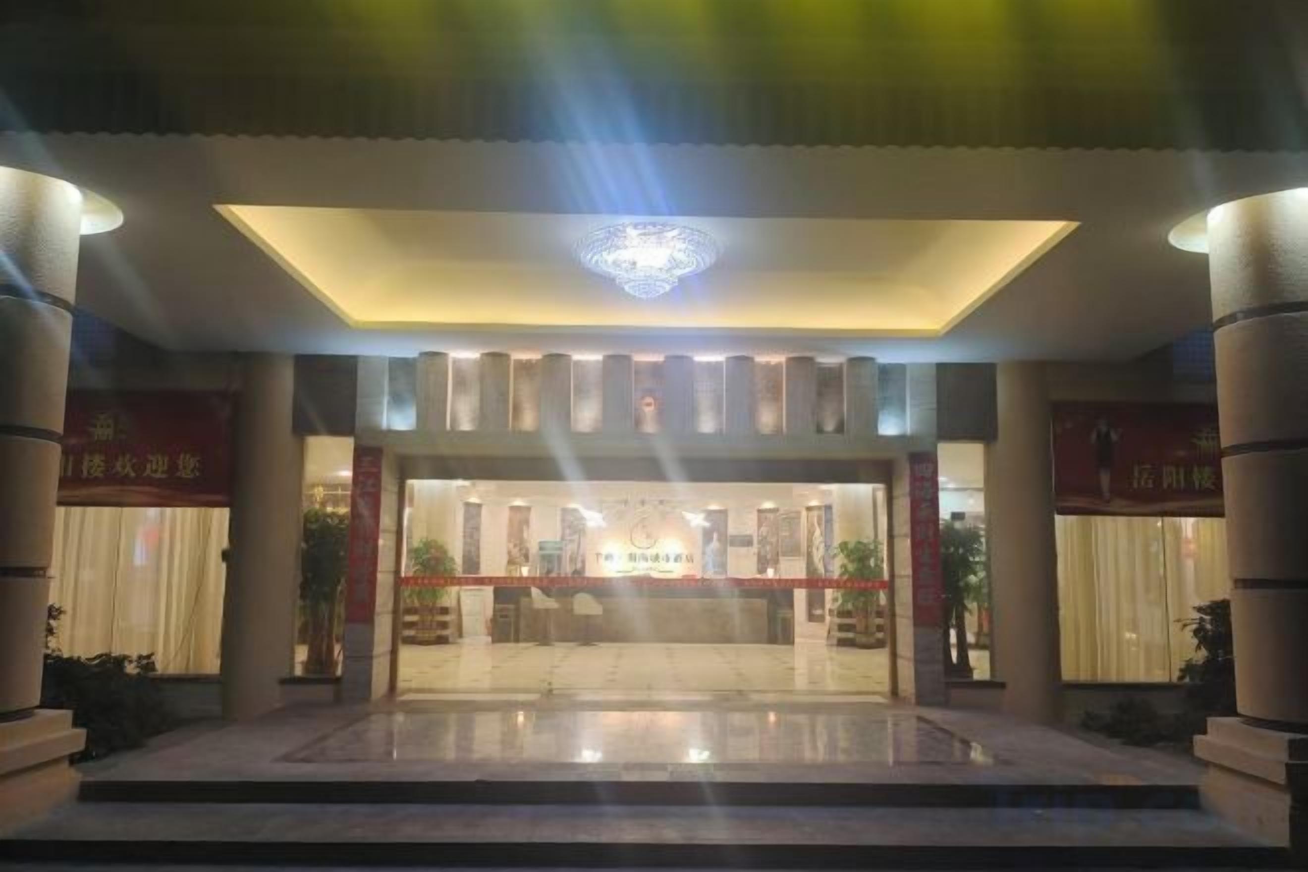 Vestíbulo de hotel con mostrador de recepción, candelabro y suelo de baldosas.