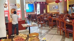 A restaurant interior with wooden chairs and tables, a person at the counter, and various food items displayed. - Nangang City Hotel (Shenzhen)