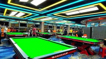 A pool hall with multiple pool tables, overhead lighting, and a patterned carpet.