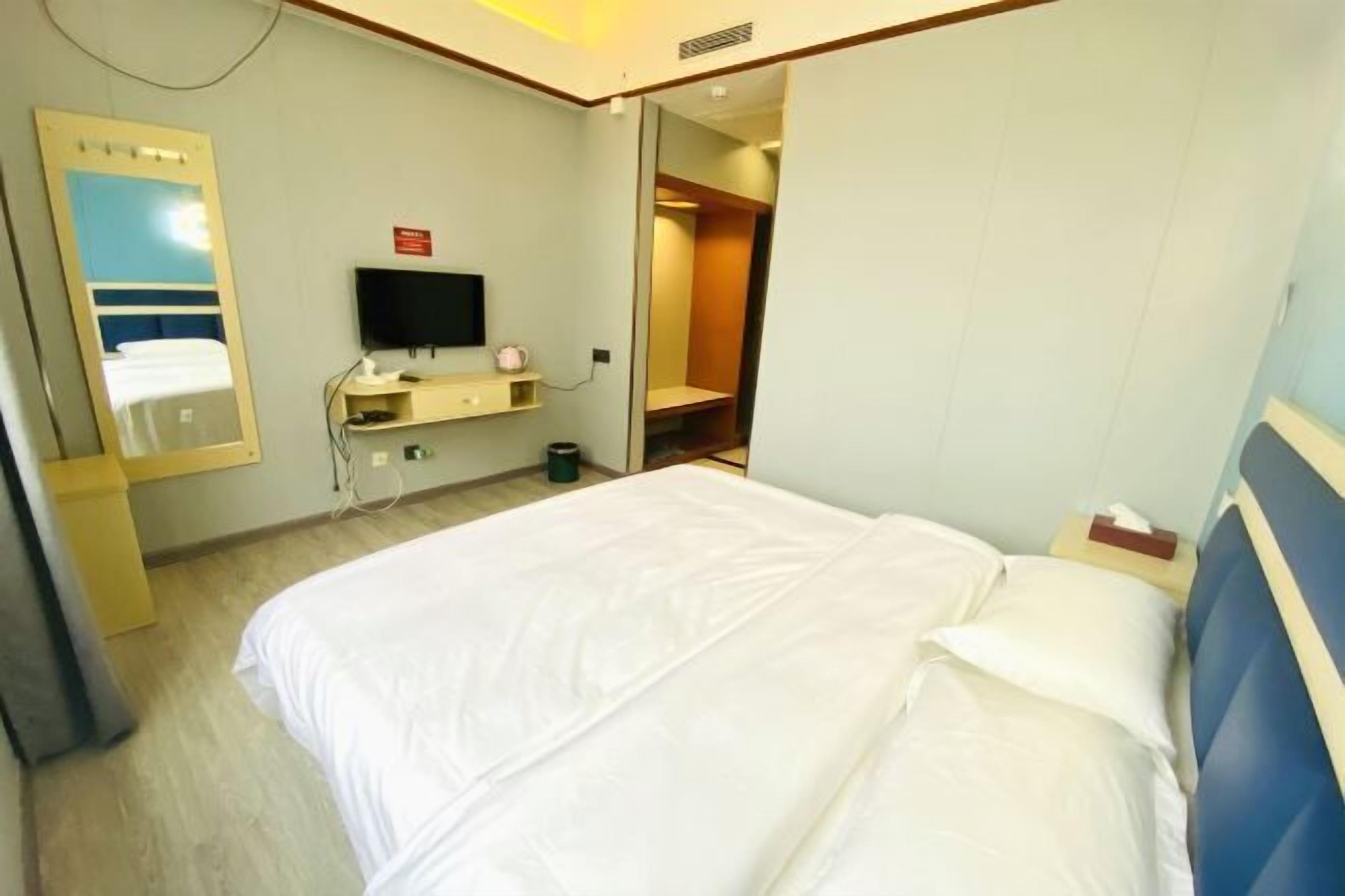 Una habitación de hotel con una cama, televisión, espejo y un escritorio pequeño.