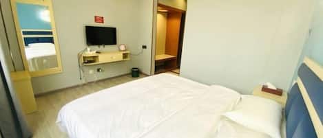 A hotel room with a bed, a television, a mirror, and a small desk.