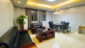 A modern living room with a sofa, a wooden coffee table, a dining table with chairs, and a potted plant. - Nangang City Hotel (Shenzhen)