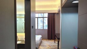 A hotel room with a bed, a window with curtains, a bathroom with a mirror, and a patterned floor. - Nangang City Hotel (Shenzhen)