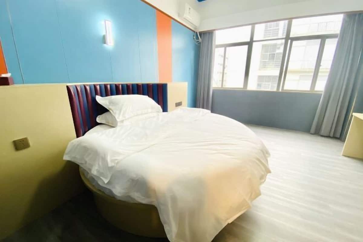 Une chambre d’hôtel avec un lit, une fenêtre avec des rideaux et un mur orné d’une bande bleue et orange.