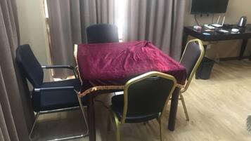 A room with a table covered by a red cloth, four chairs, a desk with a computer, and a TV.