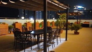 Un espace extérieur aménagé en terrasse, avec une table et des chaises, entouré de plantes en pot et d’un mur en briques.