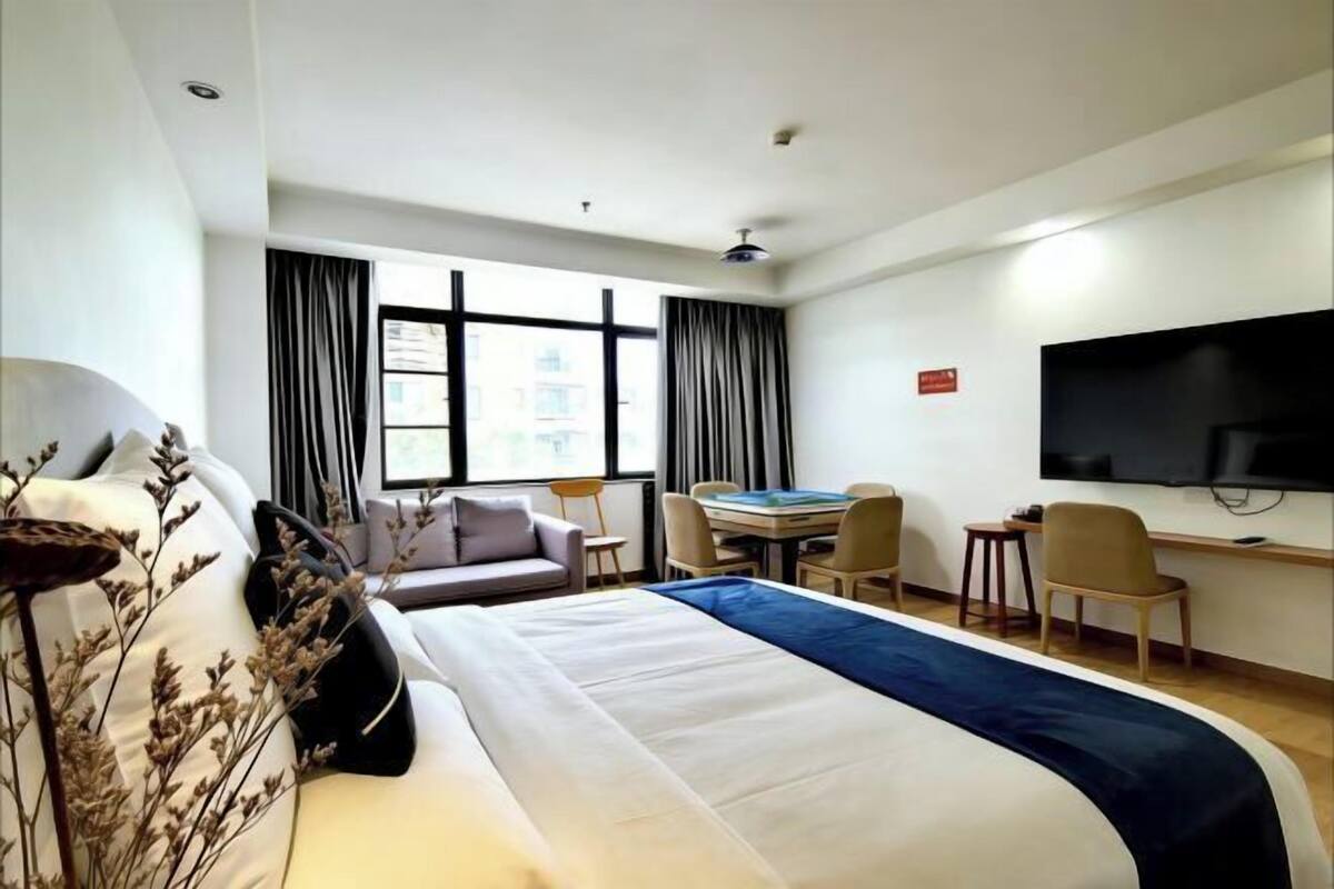 Une chambre d’hôtel avec un grand lit, un bureau, des chaises, une télévision et une fenêtre avec des rideaux.