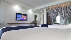 Une chambre d’hôtel avec deux lits, un téléviseur à écran plat fixé au mur et une grande fenêtre avec des rideaux.