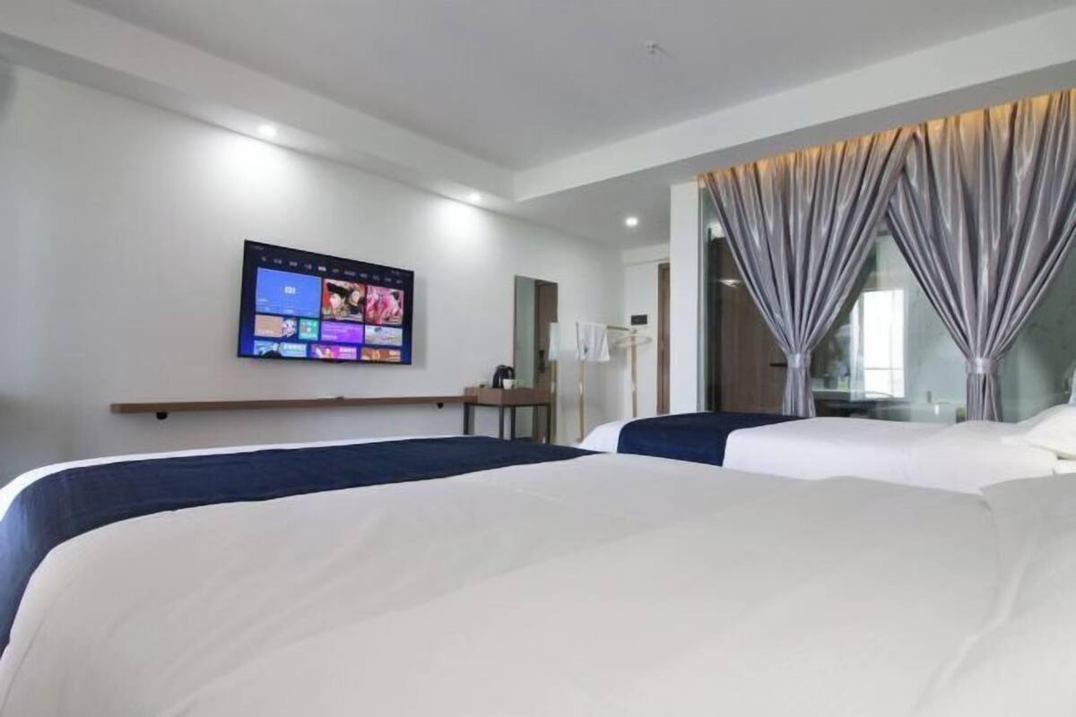 Une chambre d’hôtel avec deux lits, un téléviseur à écran plat fixé au mur et une grande fenêtre avec des rideaux.