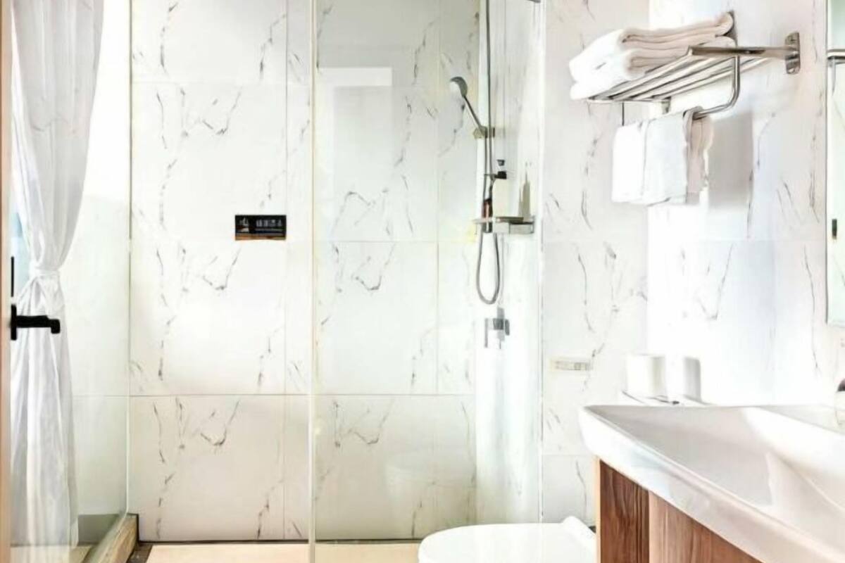 Une salle de bain moderne avec une douche à l’italienne en verre, un lavabo blanc et un porte-serviettes.