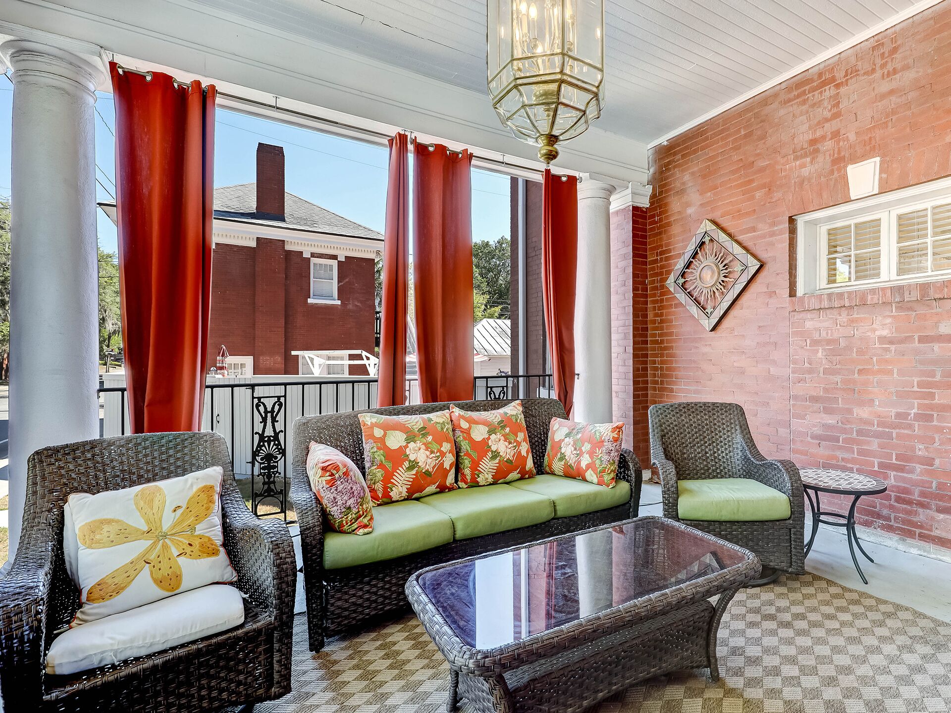 A cozy outdoor seating area with wicker furniture, a glass coffee table, and red curtains.