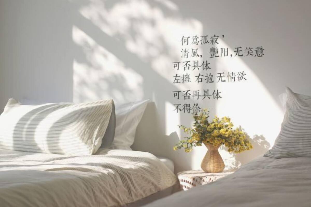 A bedroom with a bed, pillows, and a vase with flowers on a bedside table.