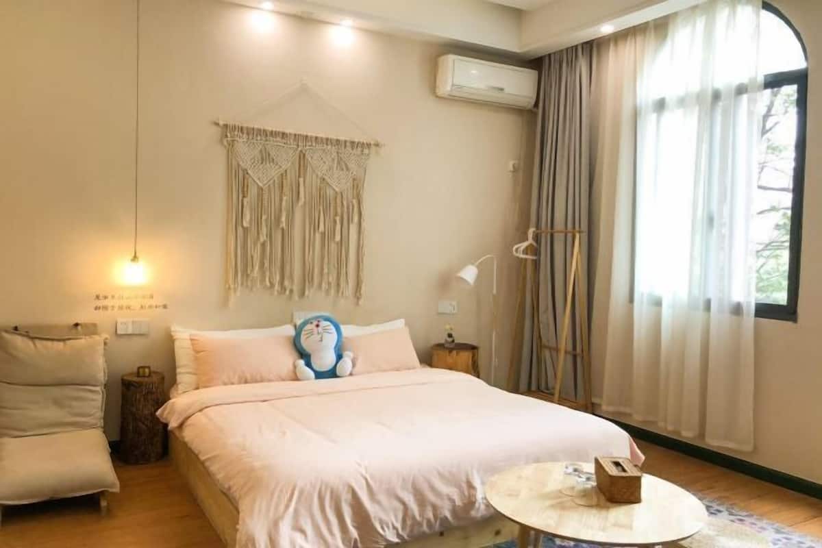 A bedroom with a bed, a bedside table, a hanging macrame curtain, an air conditioner, and a window with curtains.